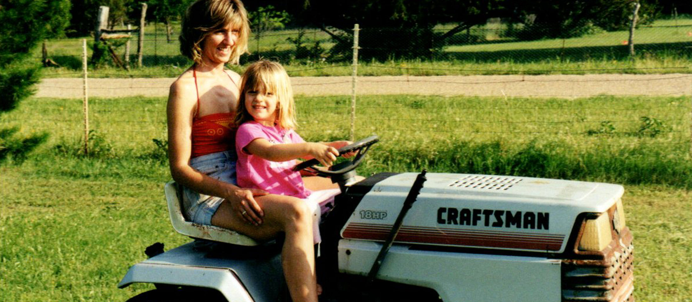 A child and her mom riding on a lawn mower.